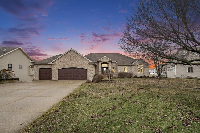 french country home with a garage, driveway, a shingled roof, a lawn, and brick siding