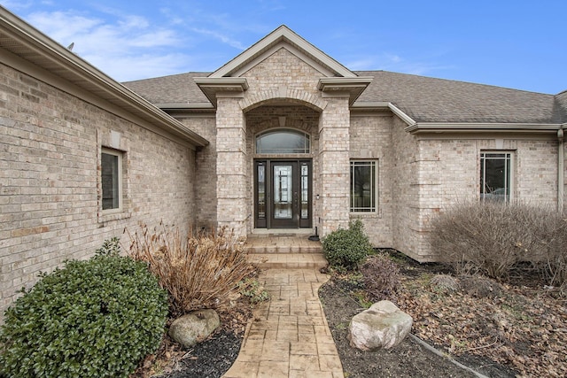 doorway to property featuring brick siding and a shingled roof