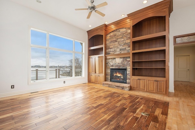 unfurnished living room featuring built in features, visible vents, a stone fireplace, and light wood finished floors