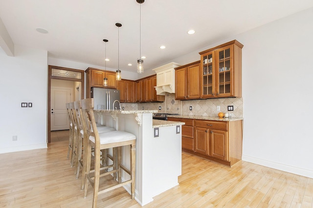 kitchen featuring a breakfast bar, backsplash, light wood-style flooring, and freestanding refrigerator