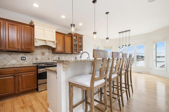 kitchen with a breakfast bar area, backsplash, light wood-style flooring, brown cabinetry, and stainless steel gas range