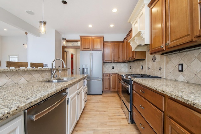 kitchen featuring light wood-style flooring, appliances with stainless steel finishes, brown cabinets, light stone countertops, and a sink