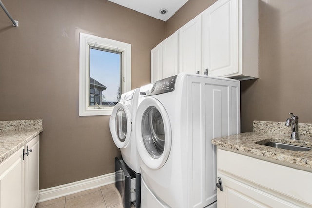 washroom featuring cabinet space, washing machine and dryer, light tile patterned flooring, a sink, and baseboards