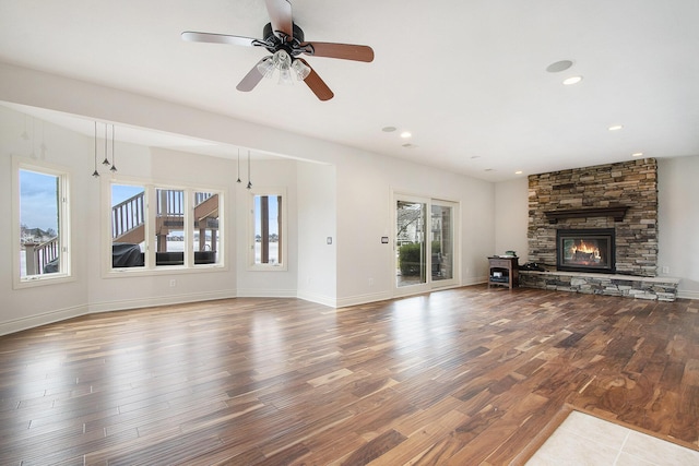 unfurnished living room with a stone fireplace, recessed lighting, wood finished floors, a ceiling fan, and baseboards