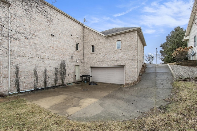 rear view of house with a garage, concrete driveway, and brick siding