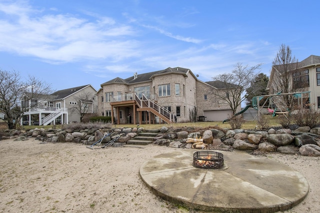 rear view of property with a playground, stairway, an outdoor fire pit, a patio area, and a deck