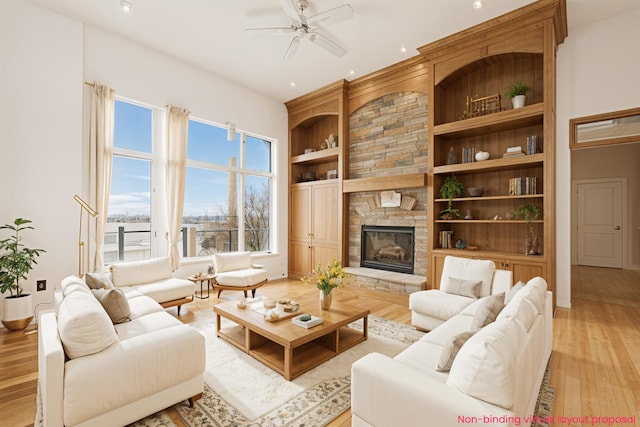 living room featuring a ceiling fan, light wood-style flooring, a stone fireplace, built in shelves, and recessed lighting