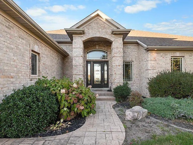 view of exterior entry featuring brick siding and a shingled roof