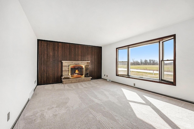 unfurnished living room with light carpet, wooden walls, a fireplace, and baseboards