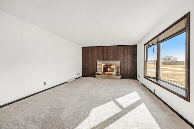 unfurnished living room featuring visible vents, baseboards, light colored carpet, wood walls, and a fireplace