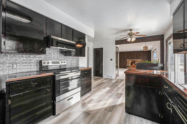 kitchen featuring visible vents, dark cabinets, stainless steel appliances, decorative backsplash, and light wood-type flooring