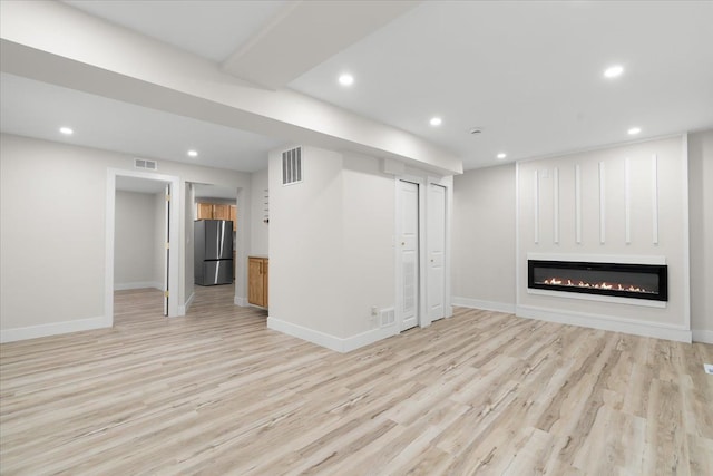 finished basement with light wood-style floors, freestanding refrigerator, visible vents, and recessed lighting