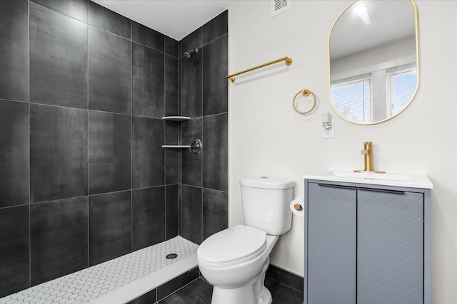 bathroom featuring visible vents, tiled shower, vanity, and toilet