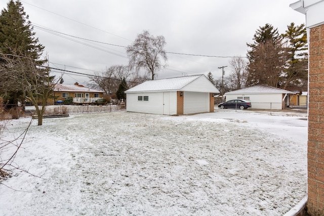 snow covered garage featuring fence and a detached garage