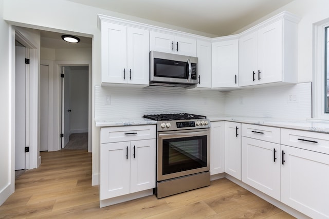 kitchen with stainless steel appliances, white cabinetry, and light wood-style flooring