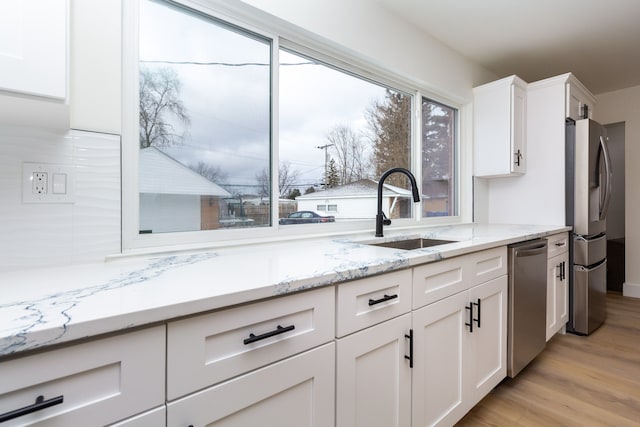 kitchen featuring white cabinets, light stone countertops, stainless steel appliances, light wood-type flooring, and a sink