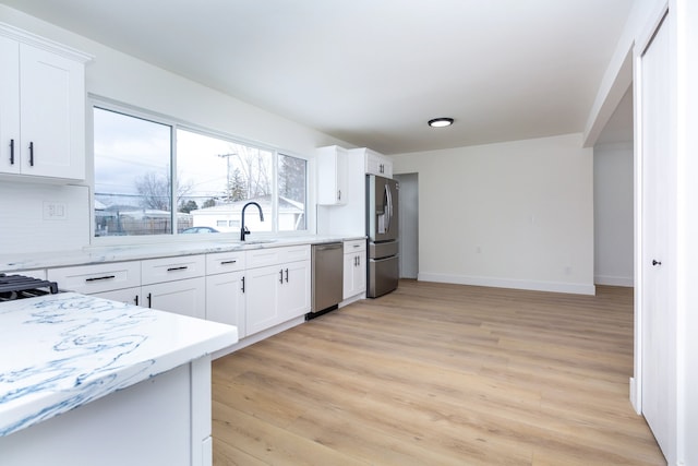 kitchen featuring light stone counters, light wood finished floors, appliances with stainless steel finishes, white cabinets, and baseboards