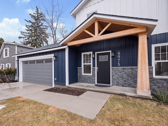 entrance to property featuring stone siding, board and batten siding, an attached garage, and driveway