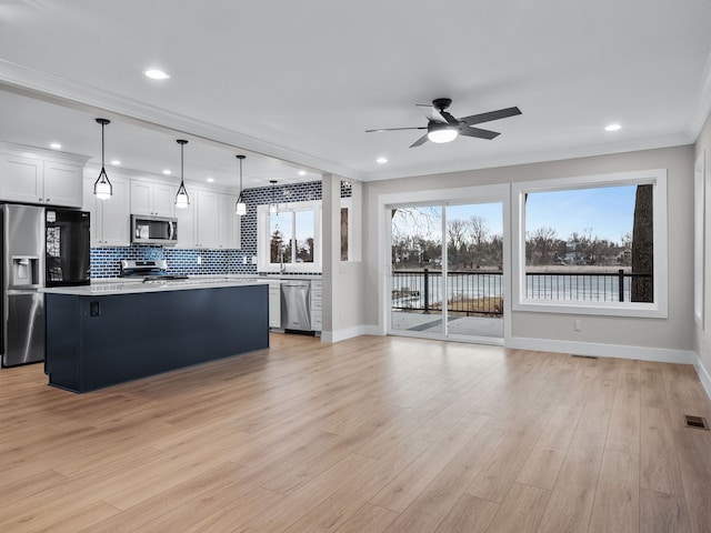 kitchen with light wood-style flooring, light countertops, appliances with stainless steel finishes, a center island, and tasteful backsplash