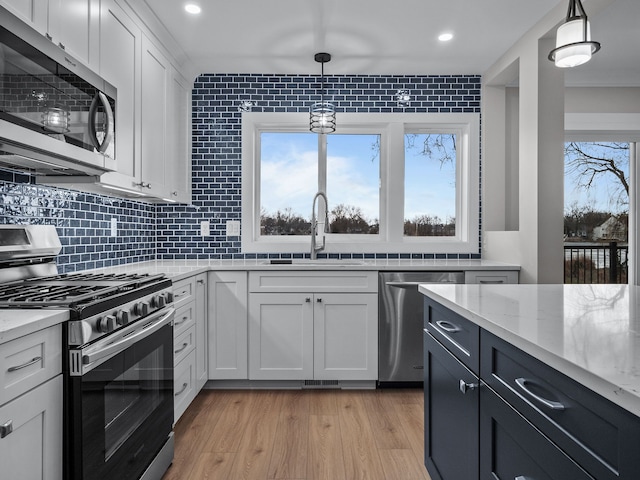 kitchen featuring a sink, white cabinetry, light wood-style floors, appliances with stainless steel finishes, and backsplash