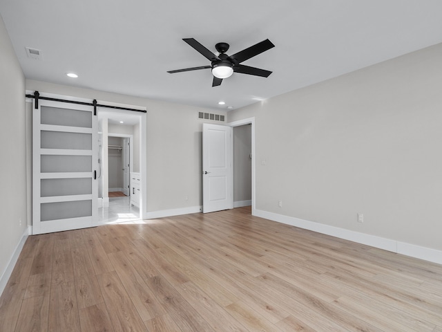 unfurnished bedroom featuring light wood finished floors, a barn door, visible vents, and baseboards