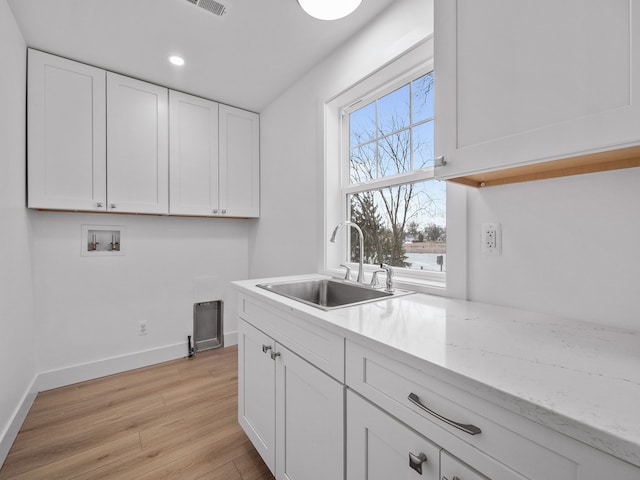 kitchen featuring light wood-type flooring, baseboards, white cabinetry, and a sink