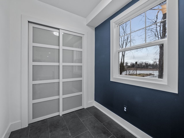 doorway to outside with baseboards and dark tile patterned flooring