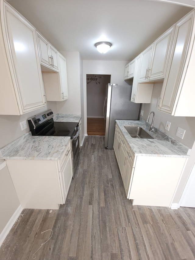 kitchen featuring light stone counters, stainless steel appliances, white cabinetry, a sink, and wood finished floors