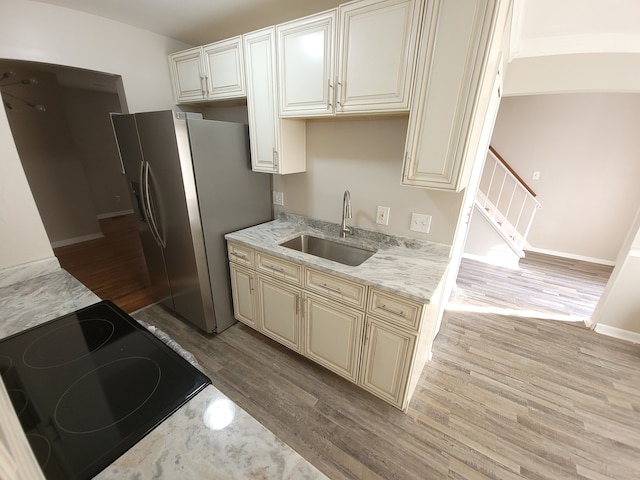 kitchen featuring stainless steel fridge, electric range oven, wood finished floors, cream cabinets, and a sink