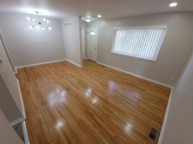 empty room featuring baseboards, visible vents, light wood-style floors, a notable chandelier, and recessed lighting