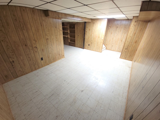 finished basement with a drop ceiling, wooden walls, and tile patterned floors