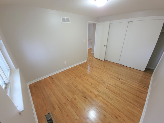 unfurnished bedroom with light wood-style floors, baseboards, visible vents, and a closet