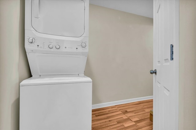 laundry room featuring stacked washer / drying machine, baseboards, wood finished floors, and laundry area