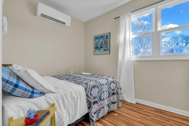 bedroom featuring a wall mounted AC, baseboards, and wood finished floors