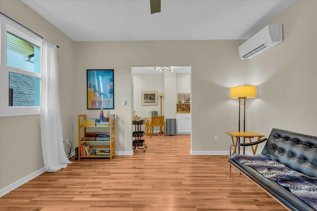 sitting room featuring light wood finished floors, baseboards, and a wall mounted air conditioner