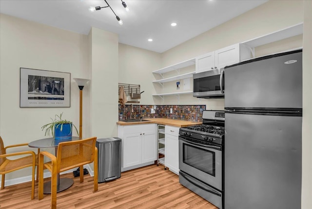 kitchen with open shelves, stainless steel appliances, white cabinets, light wood-style floors, and tasteful backsplash