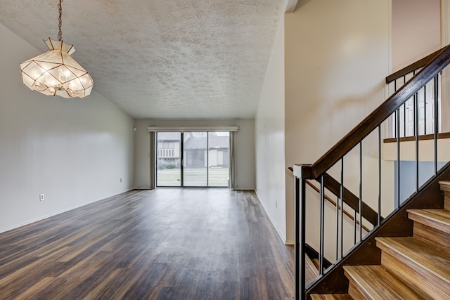 unfurnished living room with baseboards, a textured ceiling, wood finished floors, and stairs