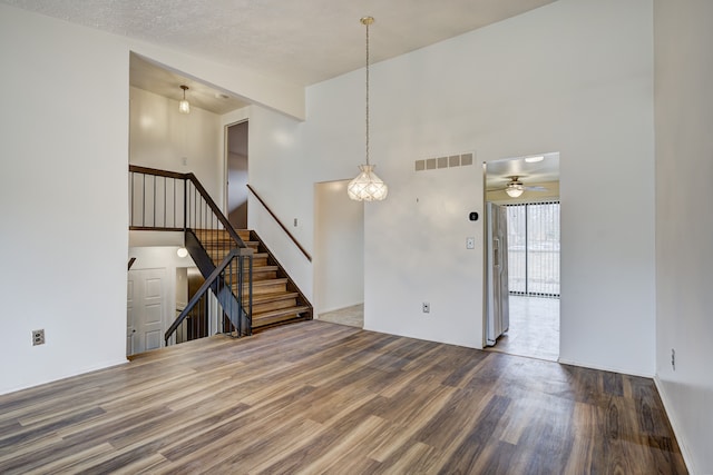 unfurnished room with stairway, wood finished floors, visible vents, and a towering ceiling