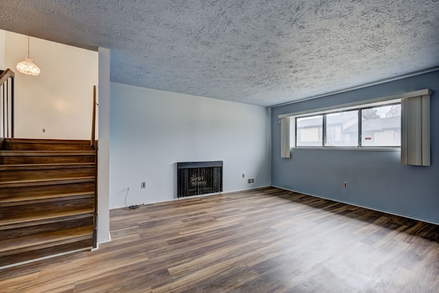 unfurnished living room with stairway, wood finished floors, visible vents, a fireplace, and a textured ceiling