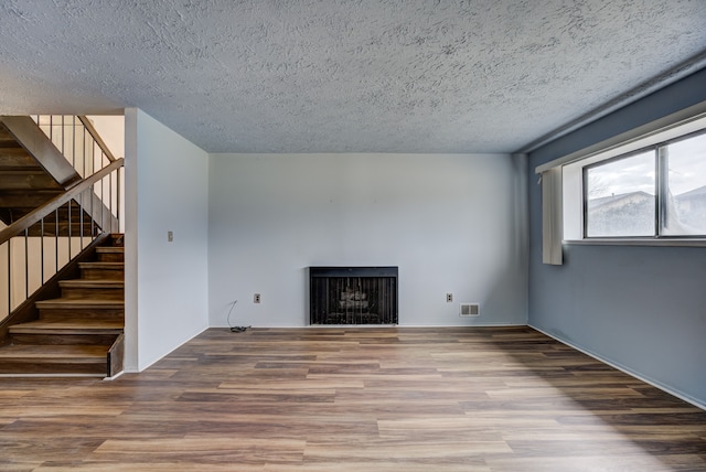 unfurnished living room with stairway, wood finished floors, visible vents, a fireplace, and a textured ceiling