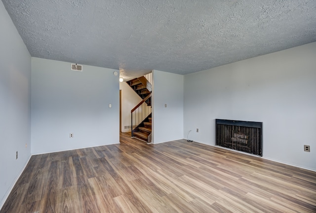 unfurnished living room featuring visible vents, stairway, a fireplace, wood finished floors, and a textured ceiling