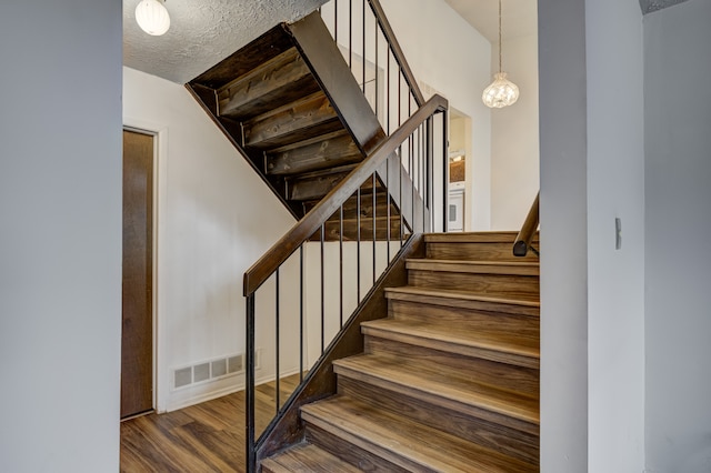 stairs featuring visible vents, a textured ceiling, and wood finished floors