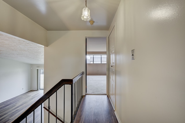 hall featuring dark wood finished floors, an upstairs landing, and a textured ceiling