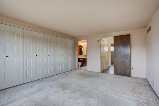 unfurnished bedroom with ensuite bath, carpet, visible vents, and a closet