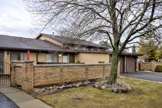 view of property exterior with a gate, a fenced front yard, aphalt driveway, roof with shingles, and a garage