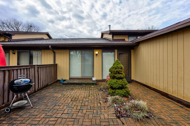 doorway to property featuring a patio area and a shingled roof