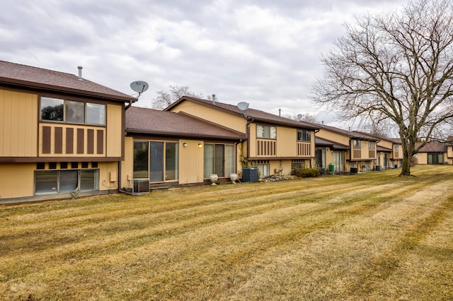 rear view of house with central AC unit, a shingled roof, and a yard