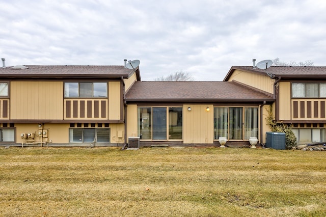 rear view of house with cooling unit, a yard, and roof with shingles