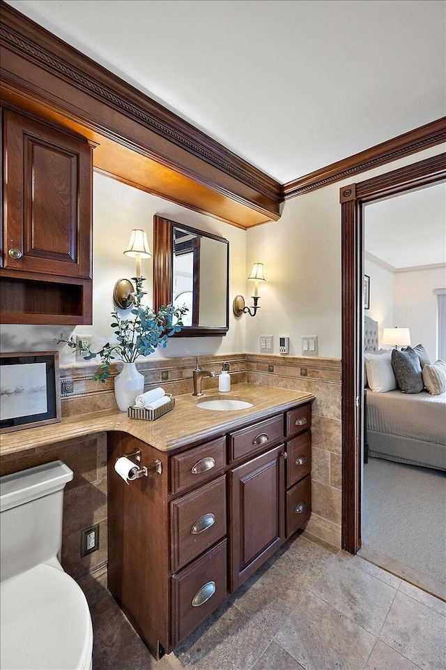 bathroom with crown molding, tile walls, toilet, wainscoting, and vanity