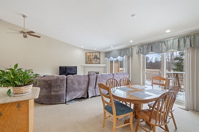 dining area with ceiling fan, recessed lighting, light colored carpet, vaulted ceiling, and a tiled fireplace